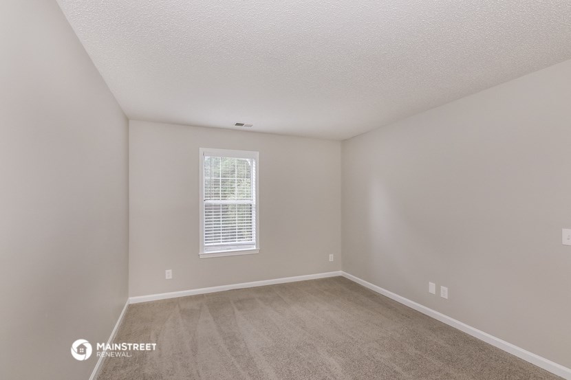 the spacious living room of an apartment with carpeting and a window