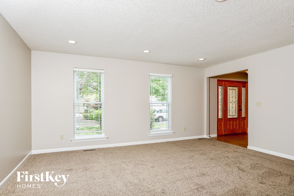 A room with a carpet floor, two windows, and a wooden door.