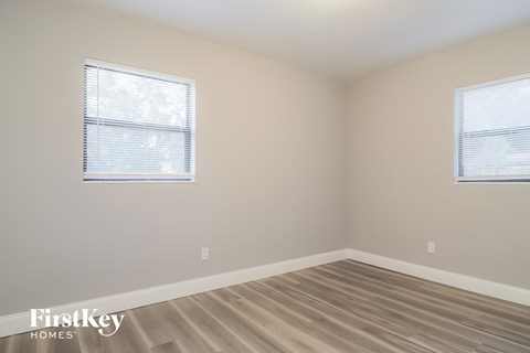 a bedroom with wood floors and two windows