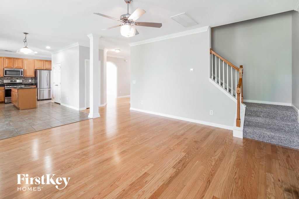 A spacious living room with wooden floors and a staircase on the right.