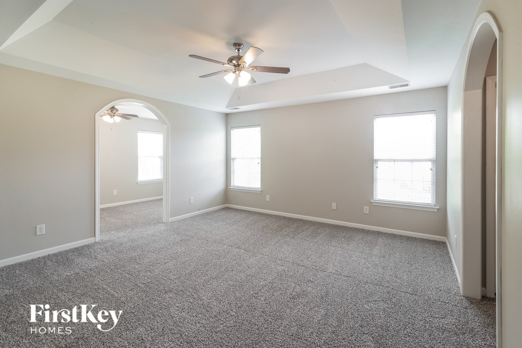 A spacious room with a ceiling fan and two windows.