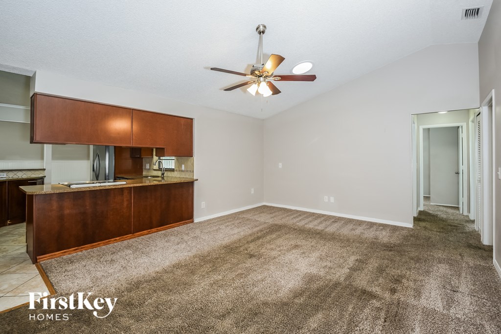 an empty living room with a ceiling fan and a kitchen