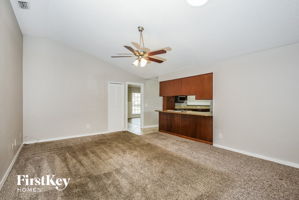 an empty living room with a ceiling fan and a kitchen