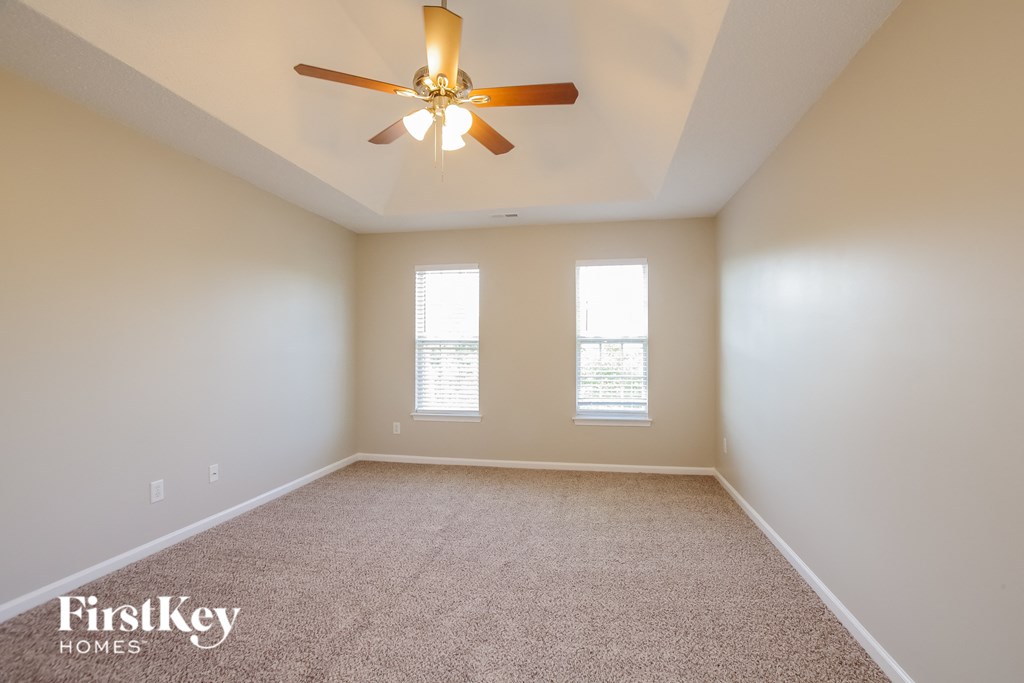 A carpeted room with a ceiling fan and two windows.