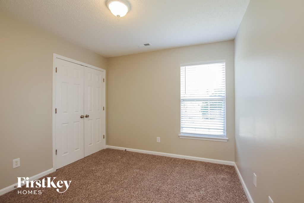 A room with a carpeted floor, a white door, and a window with blinds.