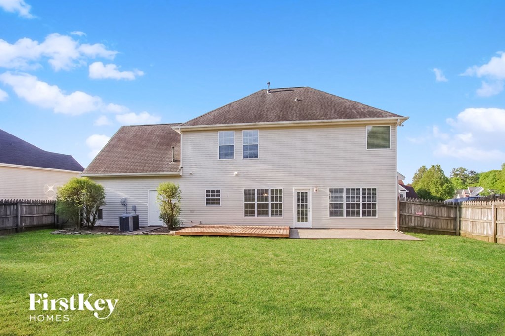 A white house with a brown roof and a fence in the front yard.