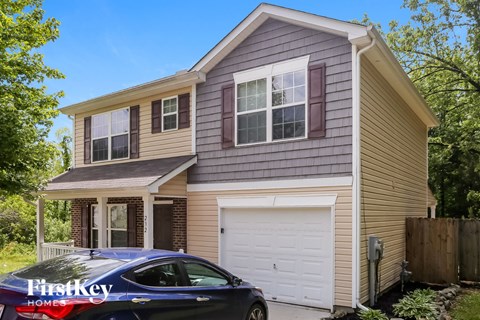 A blue car is parked in front of a two-story house.