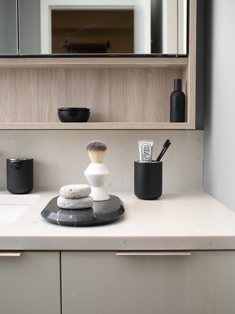 A bathroom counter with a mirror, a bowl, a brush, and a bottle.