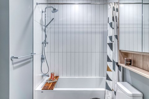A white tiled bathroom with a white bathtub and a white toilet.
