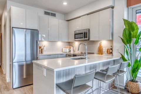 A modern kitchen with a stainless steel refrigerator, white cabinets, and a white countertop.