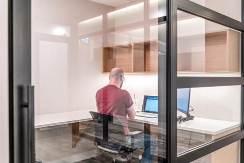 A man in a red shirt is sitting at a desk with two computer monitors.