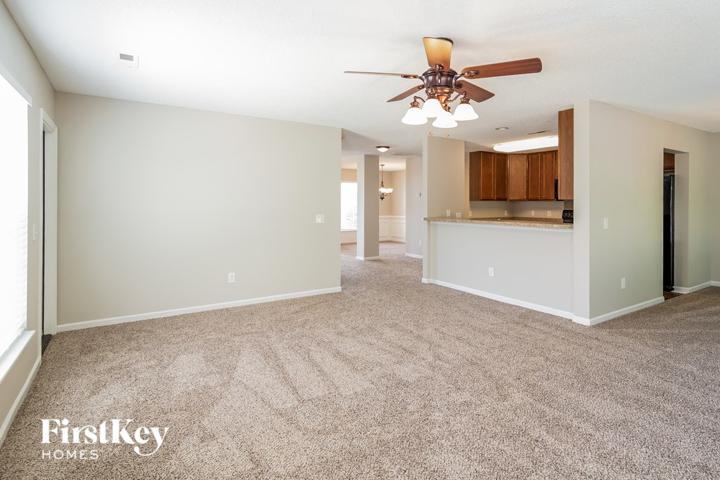 a spacious living room with carpet and a ceiling fan