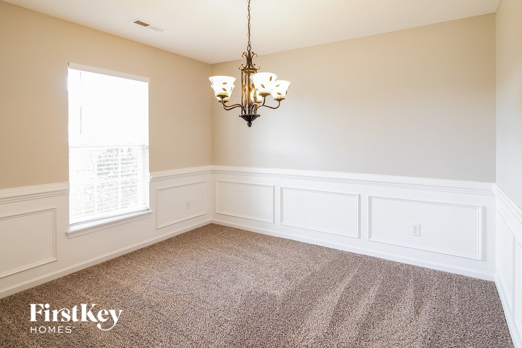 an empty dining room with white wainscoting and a chandelier