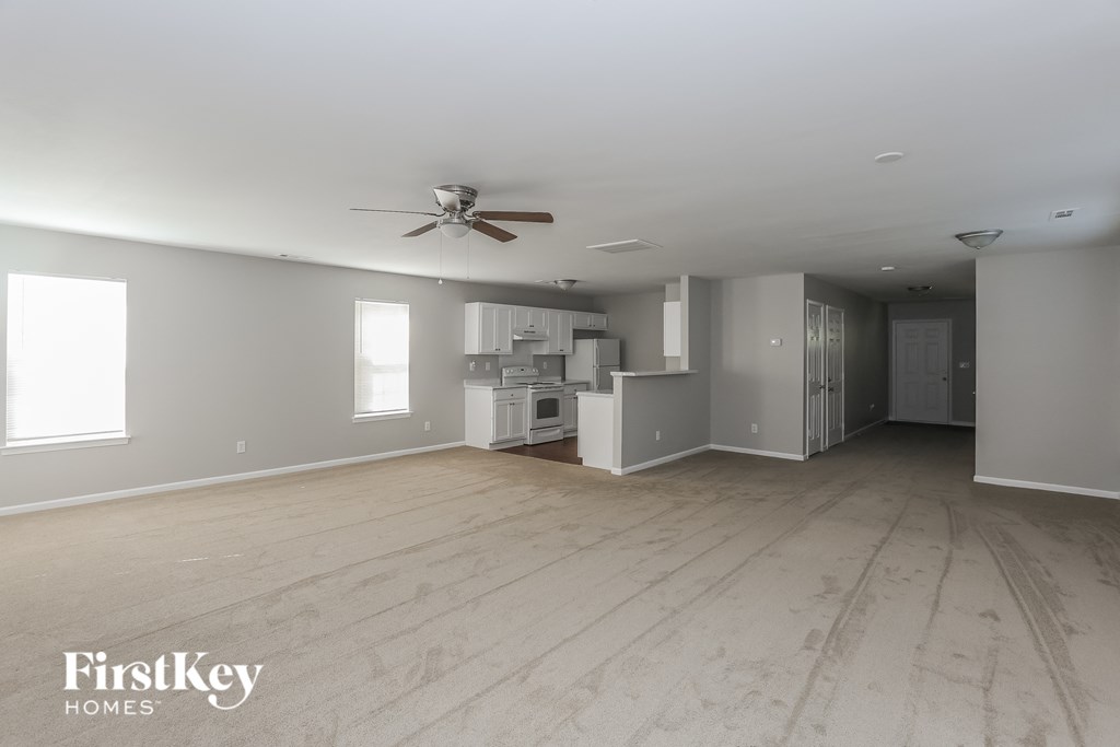 an empty living room with a ceiling fan and a kitchen