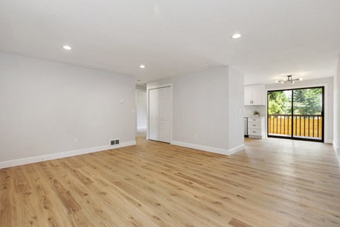 a living room with white walls and wooden floors and a door to a balcony