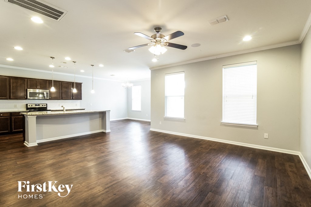 an empty living room and kitchen with wood flooring and a ceiling fan