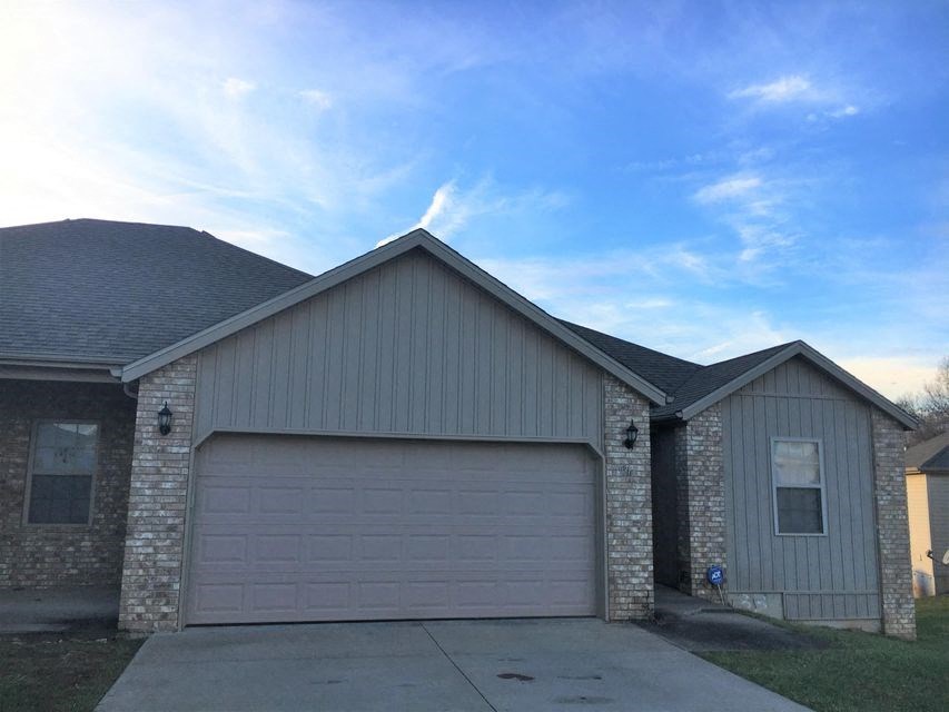 A house with a grey garage door and a brick wall.
