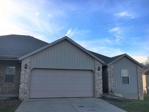 A house with a grey garage door and a brick wall.