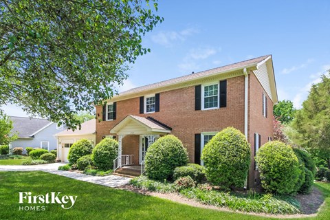 a brick house with green shutters and a lawn and trees