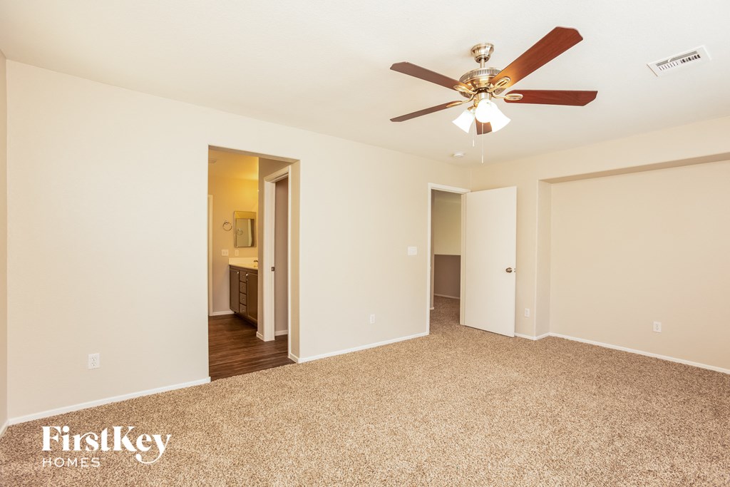 a empty living room with a ceiling fan and a hallway to a bathroom