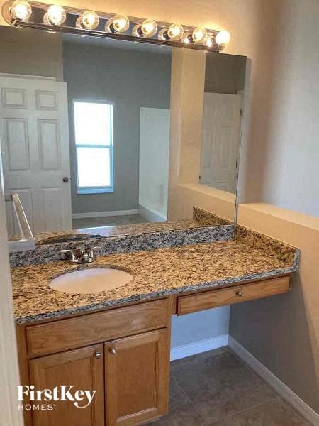A bathroom with a granite countertop and a mirror with lights above it.