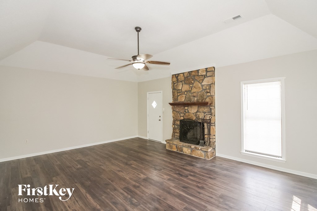 A room with a stone fireplace and a ceiling fan.