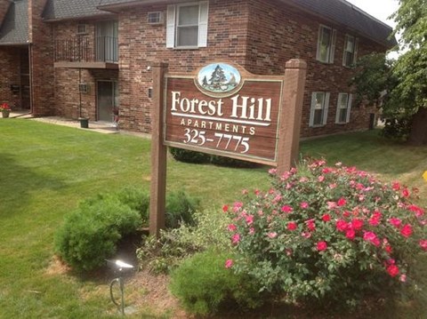 A sign for Forest Hill Apartments is in front of a brick building.