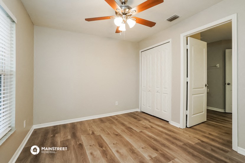 the spacious living room with wood flooring and a ceiling fan
