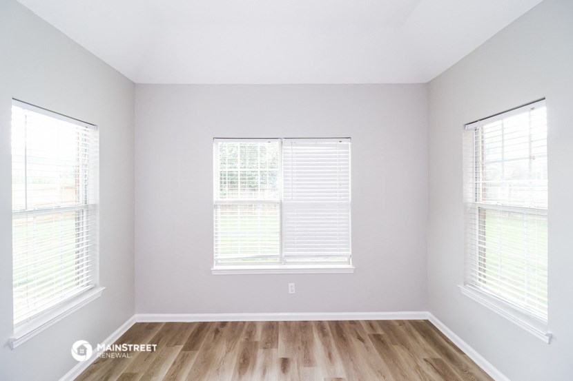 an empty room with wood floors and two windows