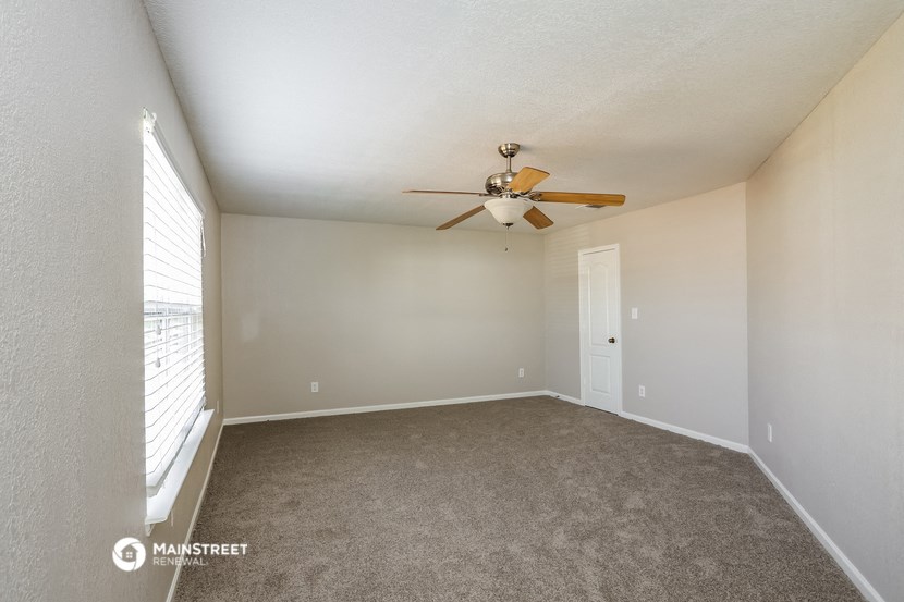 the spacious living room with ceiling fan and large window