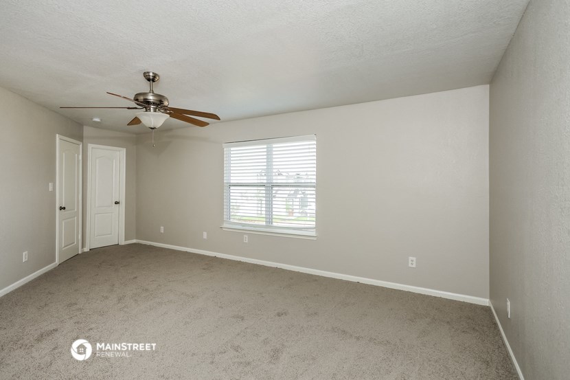 the spacious living room with ceiling fan and carpeting