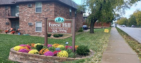 A sign for Forest Hill Apartments is in front of a brick building.