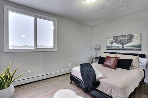 A bedroom with a bed, a potted plant, and a painting on the wall.