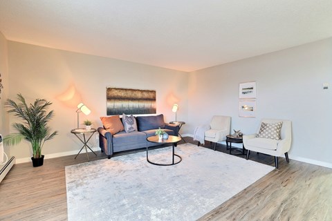 A living room with a blue couch, two chairs, and a potted plant.