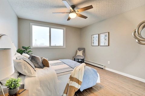 A bedroom with a bed, chair, and ceiling fan.