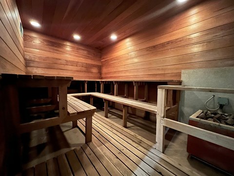 A wooden sauna with benches and a stone fireplace.