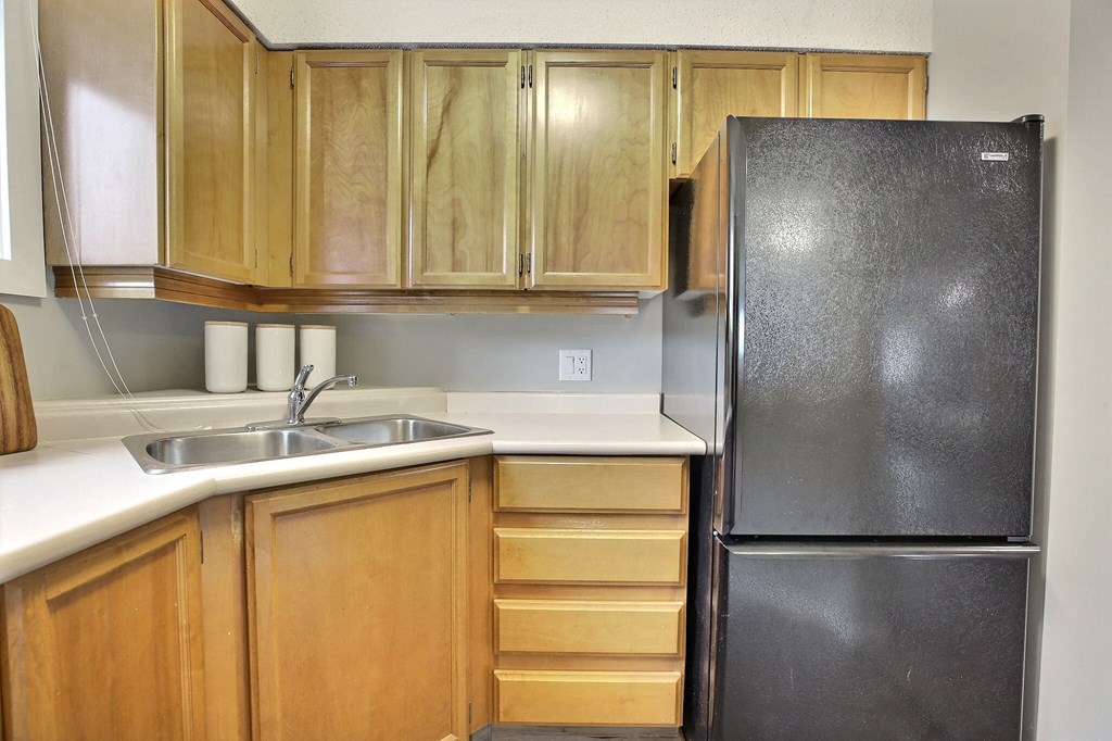 an empty kitchen with a black refrigerator and wooden cabinets