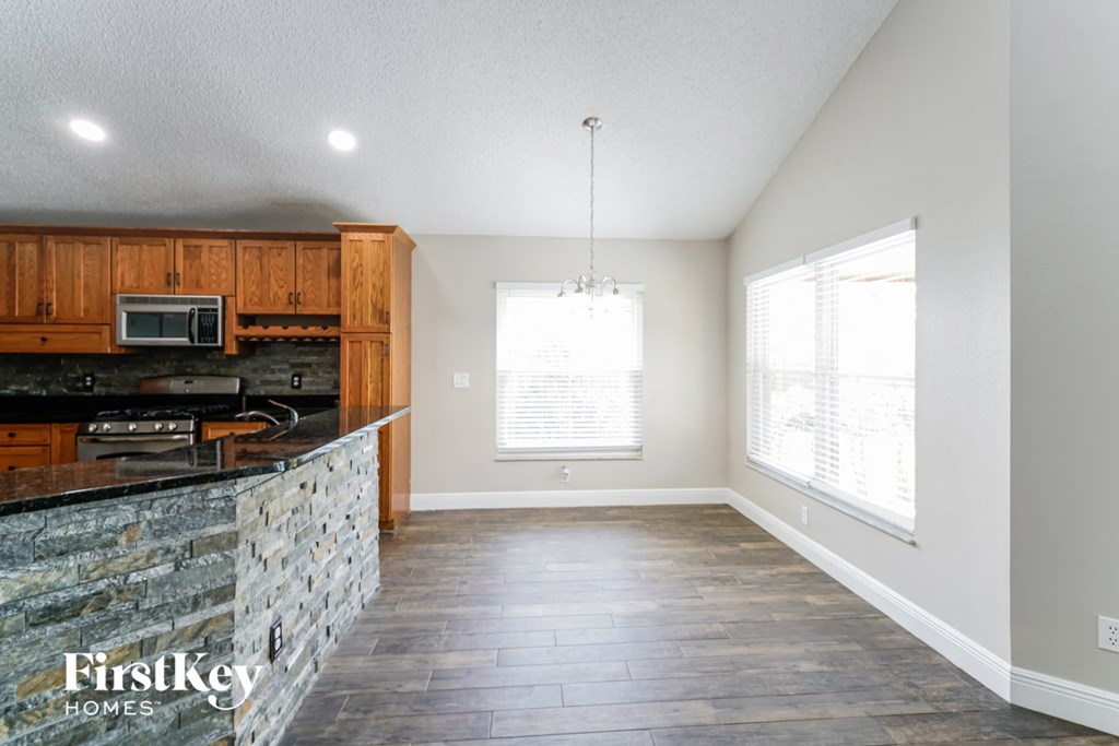 an empty living room with a kitchen with wood cabinets and a granite counter top