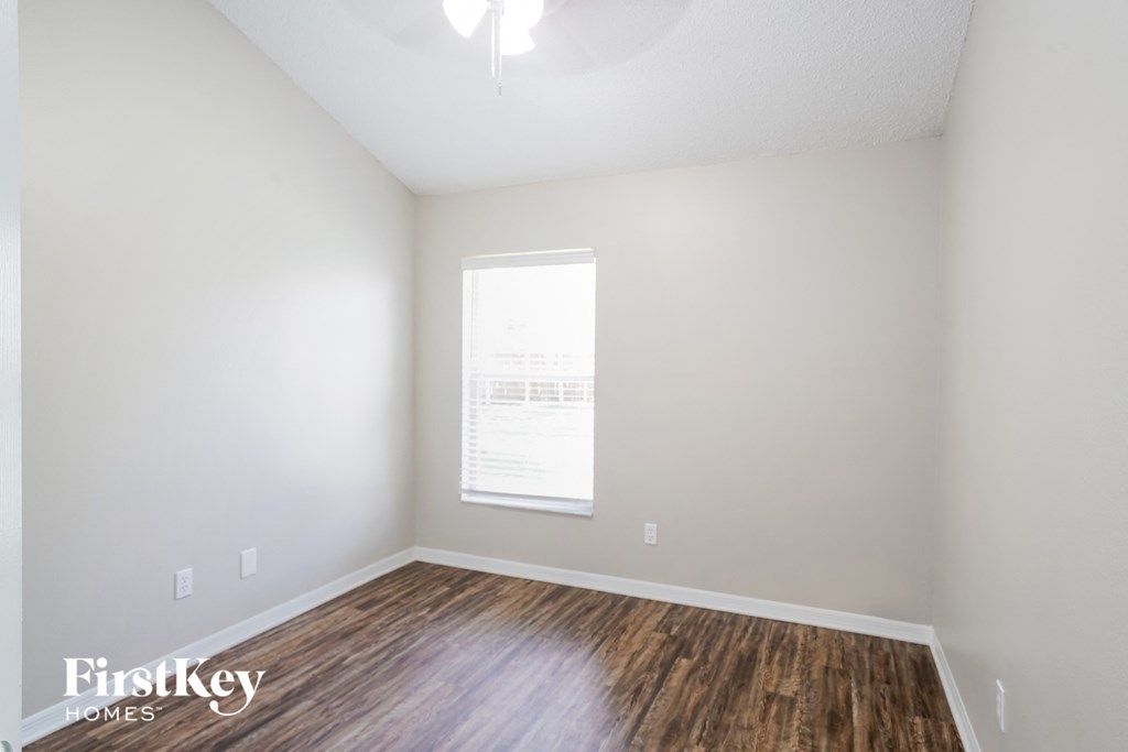 a bedroom with white walls and wood flooring and a window