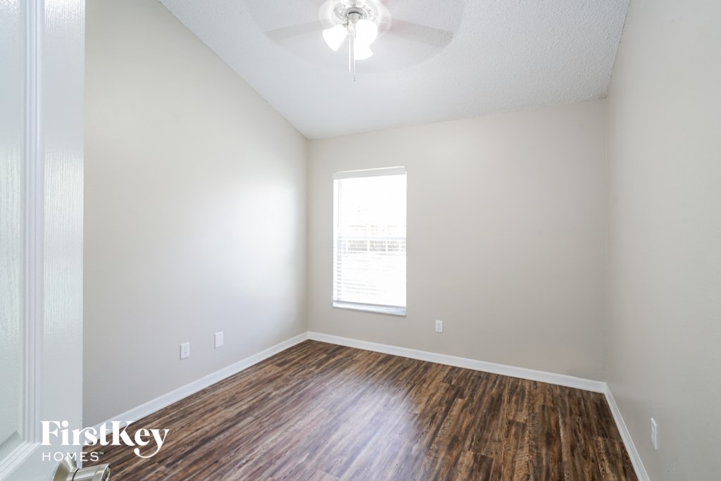 the spacious living room with hardwood flooring and a ceiling fan