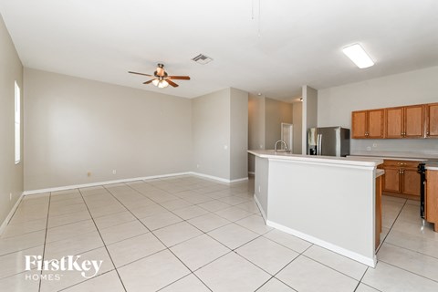 an empty living room with a kitchen and a ceiling fan