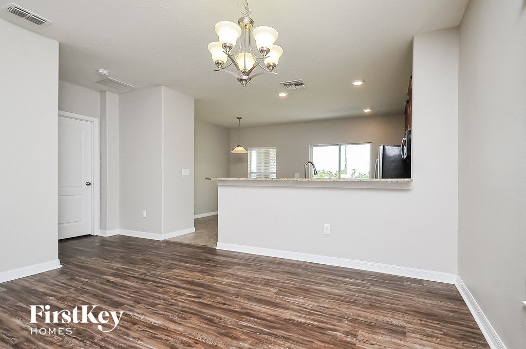 an empty living room with a kitchen and a chandelier