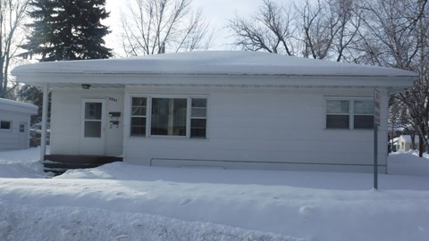 A white house with snow on the roof and ground.
