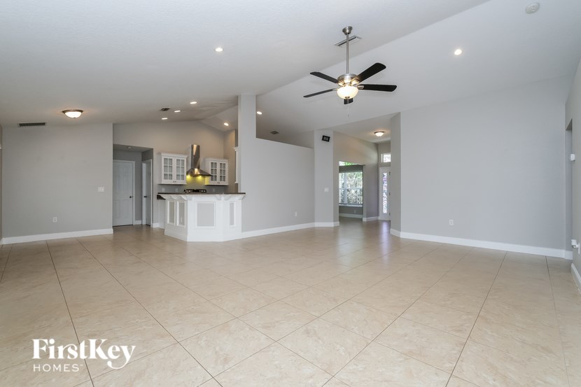 A spacious living room with a kitchen in the background and a ceiling fan.
