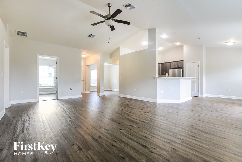 an empty living room with a ceiling fan and a kitchen