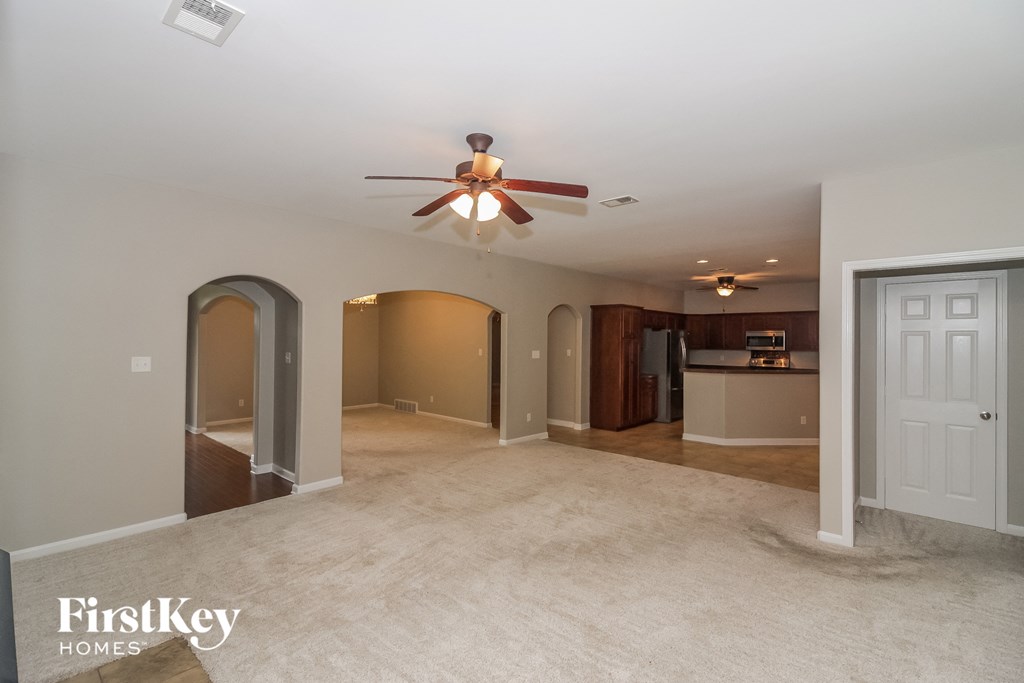 an empty living room with a ceiling fan and a kitchen