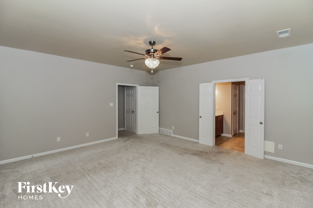 an empty living room with a ceiling fan and a white carpet