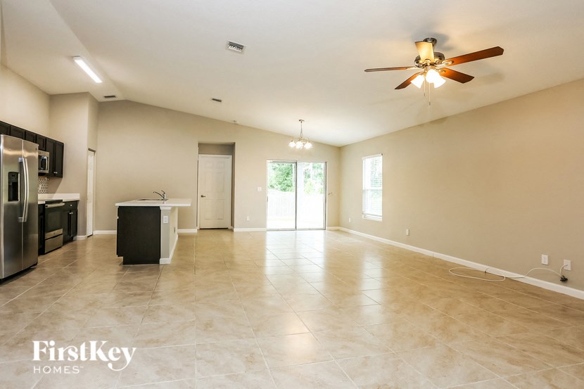 A spacious empty room with a ceiling fan and a kitchen area with appliances.