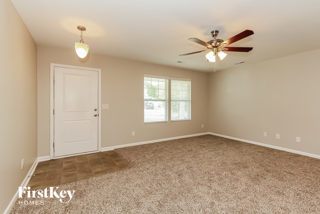 A room with a carpeted floor, a ceiling fan, and a door.