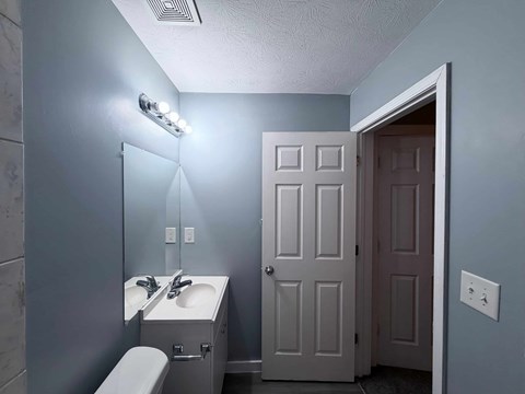 A bathroom with a toilet, sink, mirror, and light fixture.